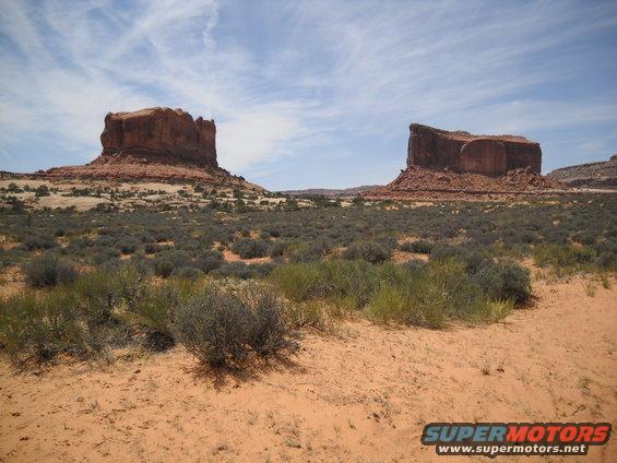 Desert landscape with red rock formations and sparse vegetation under a blue sky