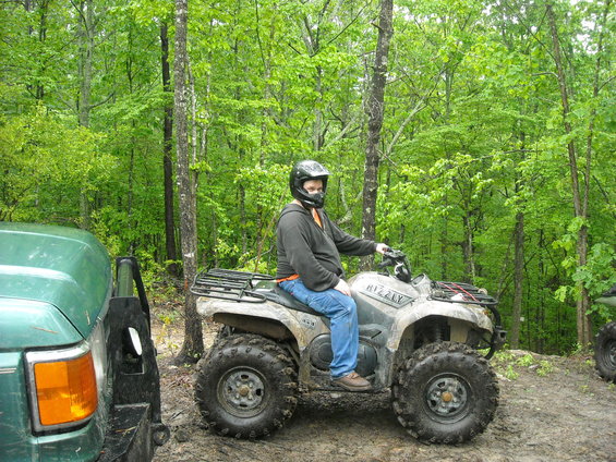 Guy on a Grizzly ATV in the woods, with a green SUV partially visible on the left