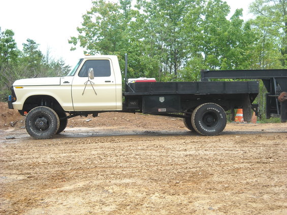Cream-colored Ford F-Series truck with a black flatbed, lifted suspension, parked on a dirt road