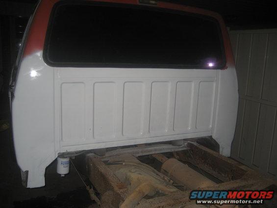 White and red truck bed, partially painted, with rusty frame visible underneath. A white filter hangs from the side