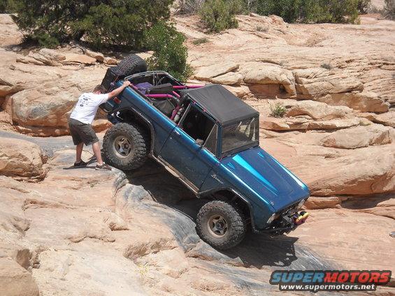 Blue 1986 Ford Bronco II climbing rocky terrain with a person pushing