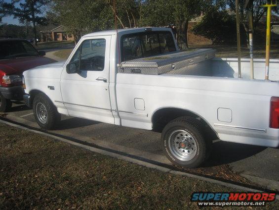 White Ford F-150 pickup truck, side view, with a toolbox in the bed and gardening tools