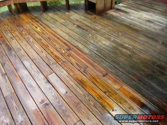 Wooden deck with half cleaned and half dirty planks, wet surface, wooden railing visible
