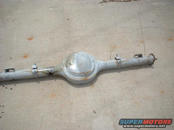 Gray rear axle assembly with a differential housing and two axle tubes, resting on a concrete surface