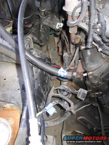 Engine compartment with hoses, wires, and engine parts. Blue tape on hoses
