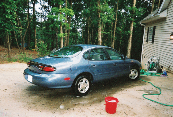 Blue 1999 Ford Taurus sedan parked on concrete driveway next to a house