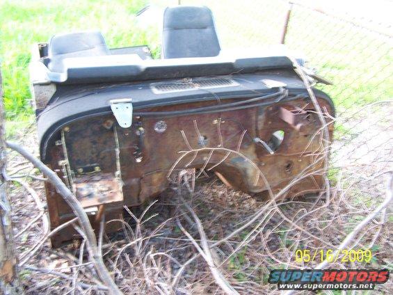 rusted vehicle front end with seats, overgrown with weeds