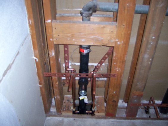Exposed plumbing pipes and copper fittings within wooden wall studs