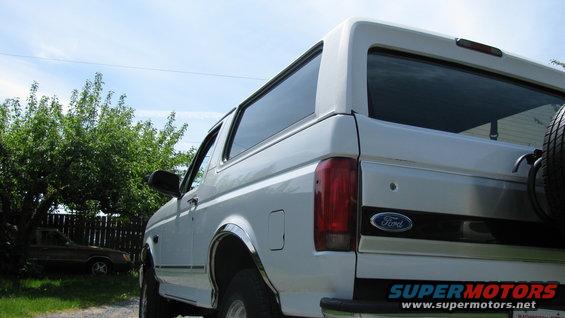 White 1996 Ford Bronco parked outside with trees and a fence in the background. Another vehicle is visible behind the fence