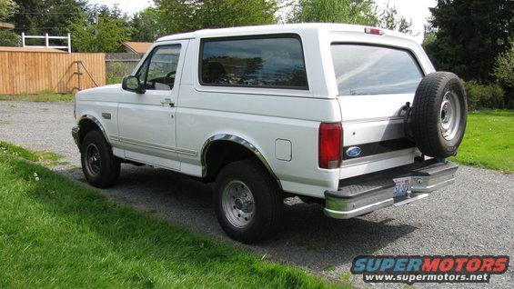 White Ford Bronco SUV parked on gravel, rear-mounted spare tire, chrome trim, visible side windows