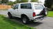 1996 Ford Bronco - A white Ford Bronco SUV is viewed from the rear three-quarter angle, parked outdoors on a gravel surface.