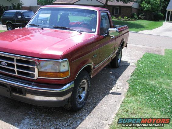 Red Ford F-150 pickup truck parked in a driveway, with a black SUV in the background