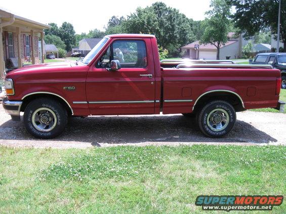 Red 1996 Ford F-150 pickup truck, side view, chrome trim, alloy wheels, parked on asphalt with grass
