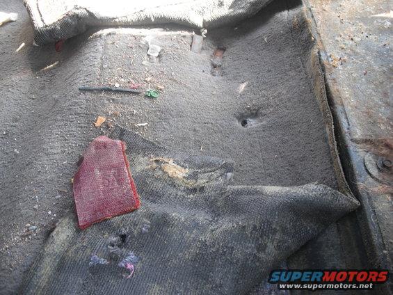 Dirty vehicle floor with torn carpet, debris, and a red fabric swatch