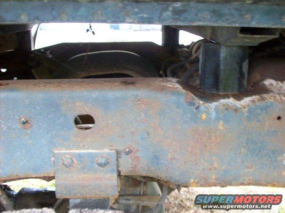 Rusted truck frame with visible suspension parts and a tire in the background