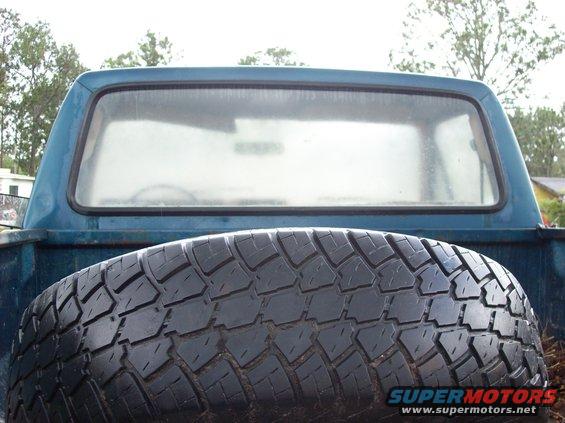 Spare tire in the bed of a blue pickup truck, seen from behind
