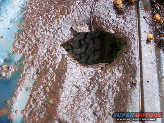 Rusted blue metal bed with a large hole revealing a tire tread below