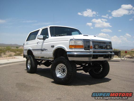 Lifted white 1996 Ford Bronco parked on asphalt with desert landscape in background