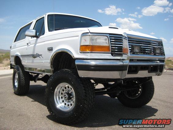 White lifted SUV with chrome wheels and grille. Another SUV is behind it