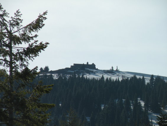 Building on a rocky, snow-dusted hilltop above a dense forest of dark green pine trees