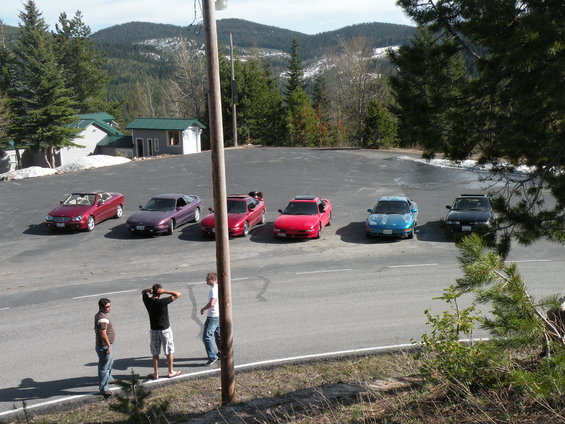 Several sports cars, including a 1989 Nissan 300ZX, parked in a lot with mountains in the background