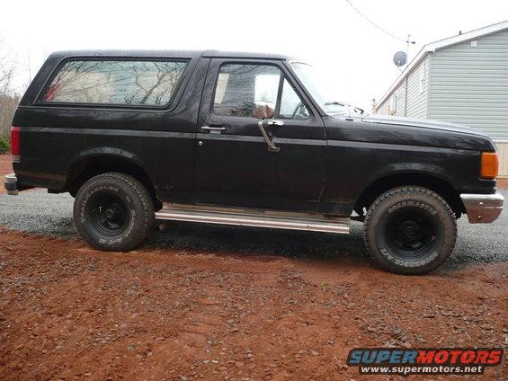 Side view of a black 1987 Ford Bronco parked on a dirt lot
