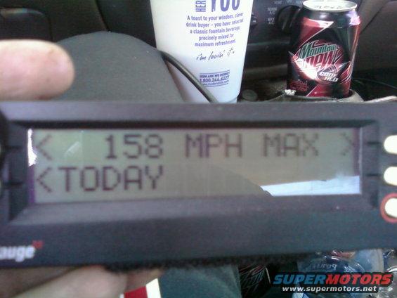 Digital gauge displaying 158 MPH MAX and TODAY, held by a hand, with a Mountain Dew can and cup in the background