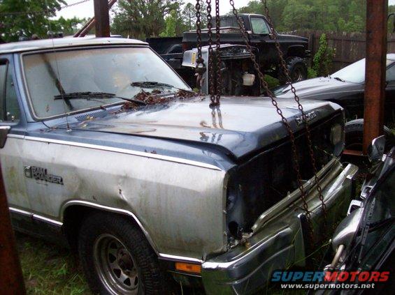 Dodge Ram pickup truck with "RAMCHARGER" on fender, hood open, chains attached, other trucks in background