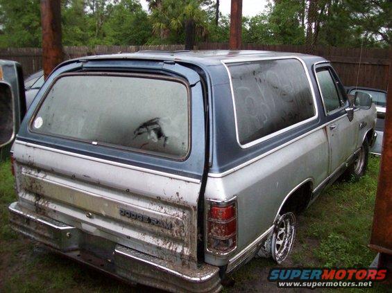 Rear view of a silver and blue Dodge Ramcharger with a broken rear window and missing hubcap