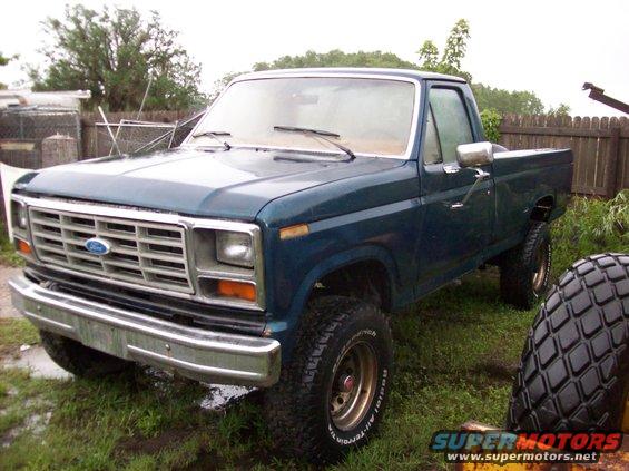 Blue Ford F-250 pickup truck with aftermarket wheels and tires parked in a grassy yard