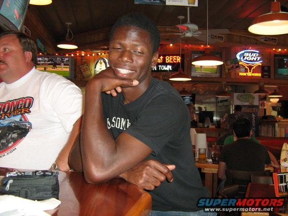 Two men sitting at a bar, one wearing a Bronco River t-shirt