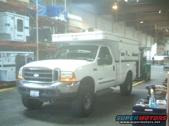 White Ford pickup with a camper shell parked indoors, near shelves with storage