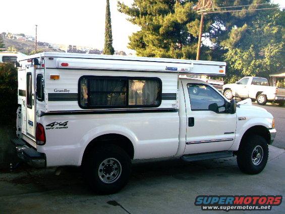 White Ford F-250 pickup truck with a Grandby camper shell, side view, 4x4 decal on rear fender