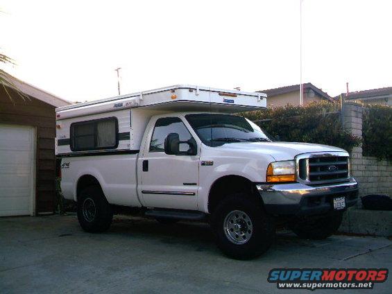 White pickup truck with a camper shell parked in a driveway. The truck has a chrome grille and bumper