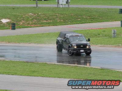 Black Chevrolet Silverado pickup truck with camper shell on wet asphalt track