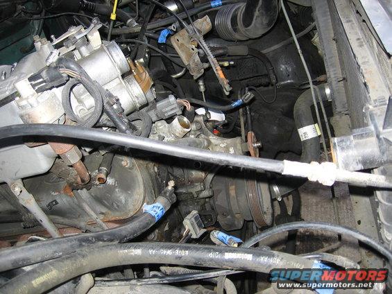 Engine bay with hoses, belts, and various components visible. Some blue tape on hoses