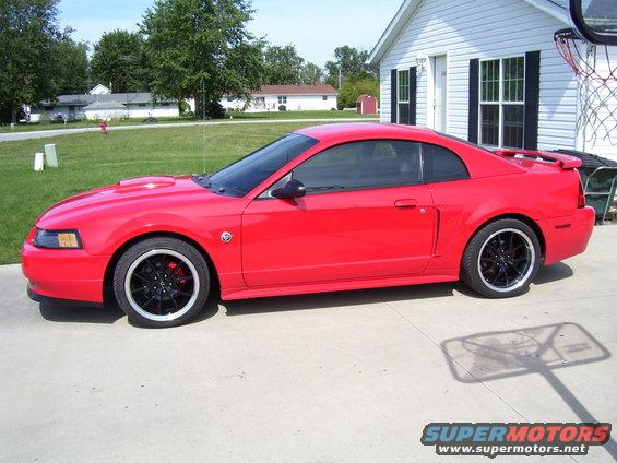 Red Ford Mustang parked on driveway in front of a house. It has black rims and a hood scoop