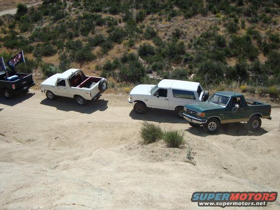 Green pickup truck and white SUVs on dirt road