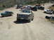 1986 Ford Bronco - Multiple off-road vehicles gather on a dusty trail, with a tan 1980 Ford Bronco prominently in the foreground.