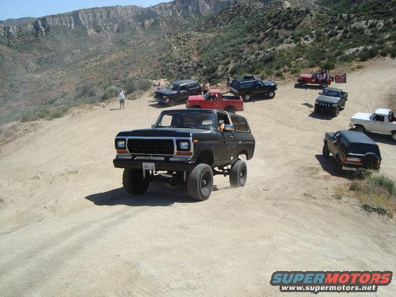Black Ford Bronco driving on a dirt road with other trucks and SUVs behind it