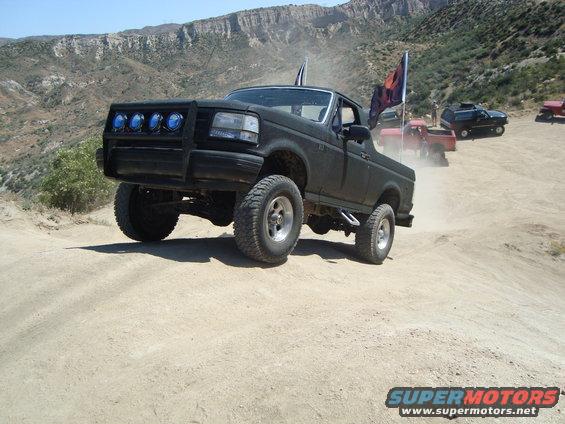 Black lifted 1992 Ford F-150 driving on a dirt trail with other vehicles behind