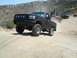 1986 Ford Bronco - A lifted black 1992 Ford F-150 navigates a dusty off-road trail, with other vehicles following in the background.