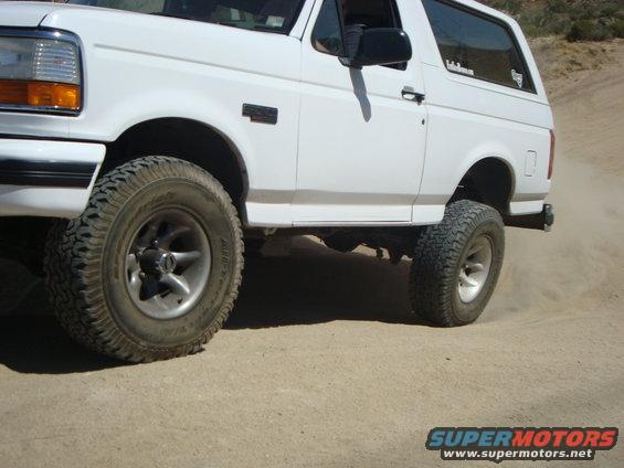 White Ford Bronco with off-road tires driving on a dirt road