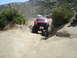 1986 Ford Bronco - This red SUV is navigating a challenging off-road trail with other vehicles in the distance.