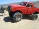 1986 Ford Bronco - Modified red Ford Bronco with oversized tires sits on a dirt road under a clear sky.