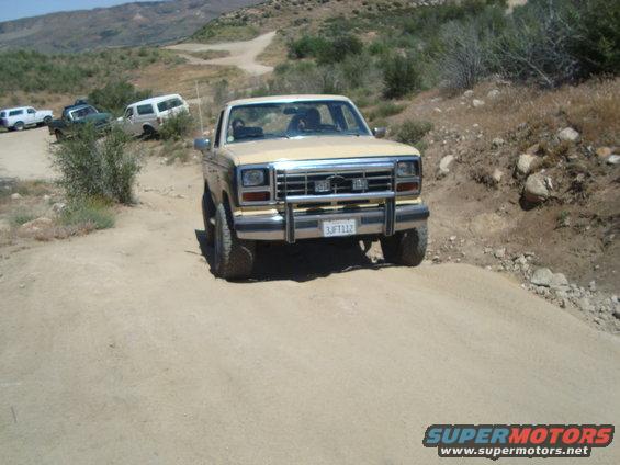 1986 Ford Bronco driving on a dirt trail with other vehicles in the background