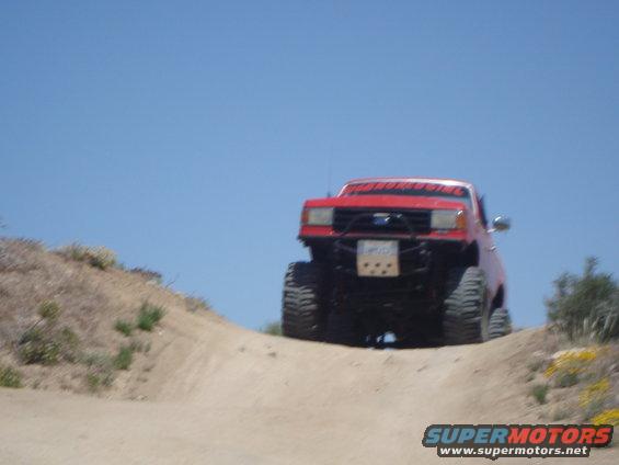 Red off-road truck with large tires climbing a dirt hill under a clear blue sky