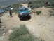 1986 Ford Bronco - A teal Ford F-Series truck navigates a challenging off-road trail with other vehicles present.