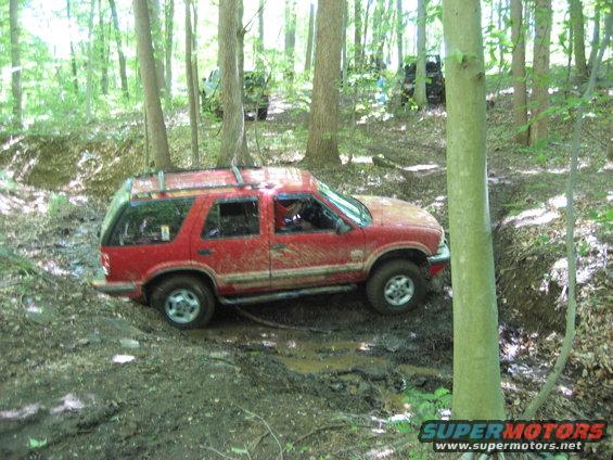 Red SUV stuck in mud, trees and other vehicles in background