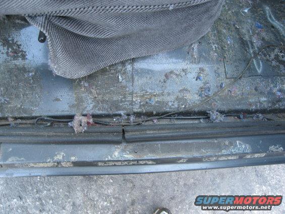Car floor with debris and exposed wires under a seat cushion